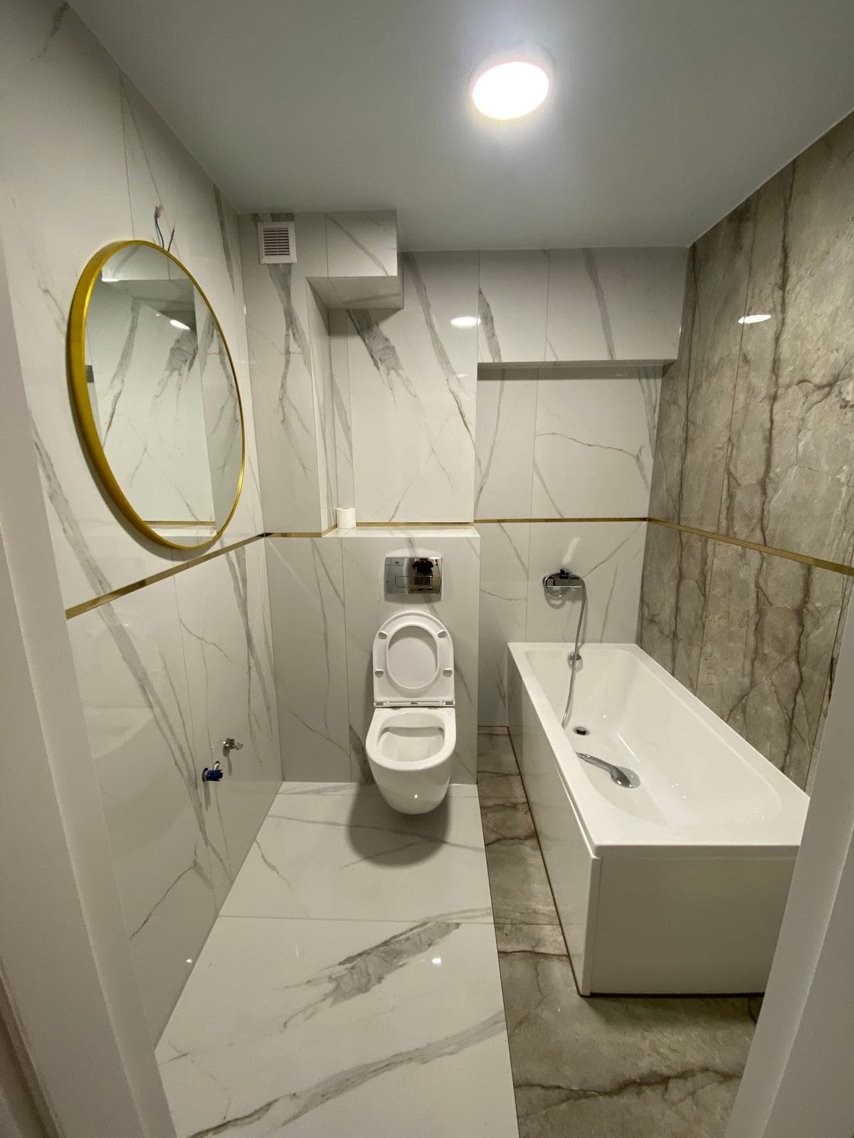 Elegancka łazienka po remoncie pod klucz w Szczecinie - gres imitujący marmur, wanna, podwieszane WC, złote listwy i okrągłe lustro w złotej ramie od STmaster.