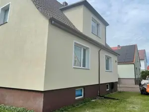 Ściana domu z jednolitym kremowym tynkiem po malowaniu całej płaszczyzny elewacji, bez widocznych łat