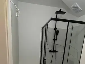 Łazienka po remoncie z kabiną prysznicową w czarnych profilach, jasnymi płytkami i wentylatorem wyciągowym pod sufitem