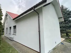 Narożnik i pas pod okapem domu z białym tynkiem, rura spustowa na narożniku - typowe miejsca kucia dzięcioła