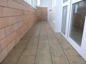 Zabudowana loggia z płytkami drewnopodobnymi ułożonymi z przesunięciem na podłodze i płytkami imitującymi cegłę na ścianie pod oknami