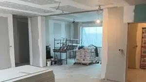 Mieszkanie w trakcie remontu kapitalnego: nowe ścianki i sufit z płyt g-k ze szpachlowanymi łączeniami, rusztowanie warsztatowe, paleta worków z zaprawą i stos płyt na posadzce