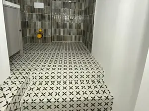 Strefa prysznica walk-in w trakcie remontu łazienki z ciemnymi cegiełkami na ścianach i wzorzystymi płytkami na podłodze i stopniach