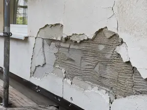 Uszkodzony tynk cienkowarstwowy na ociepleniu - odsłonięta siatka z włókna szklanego i klej zbrojący